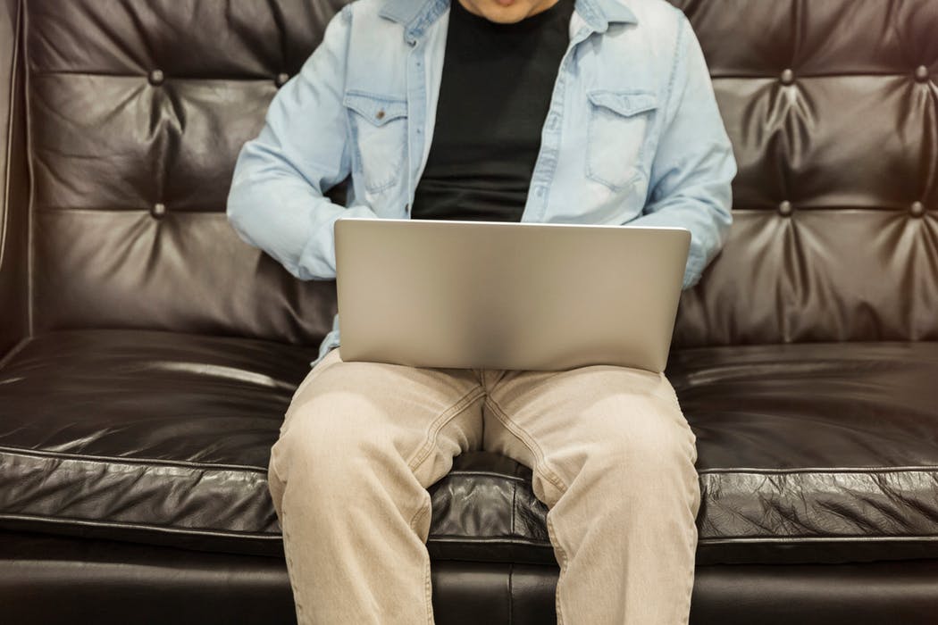 man using laptop while sitting on a leather sofa